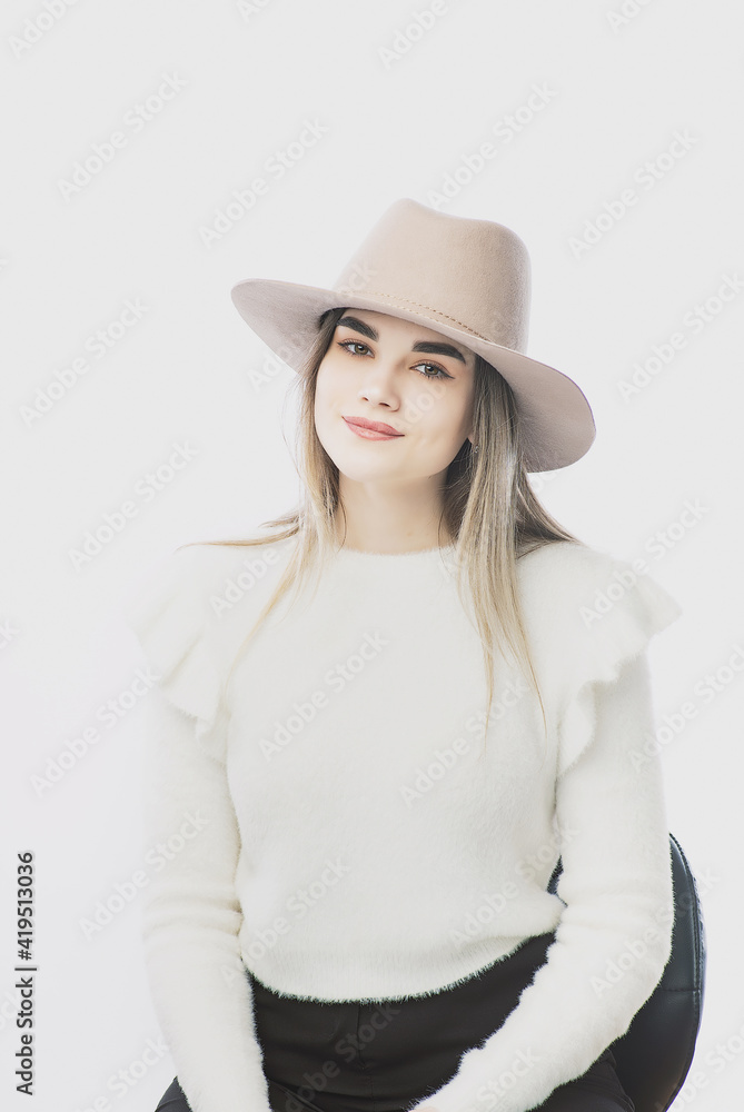 girl in a white sweater posing in a felt hat on a light background girl in a white sweater posing in a felt hat on a light background