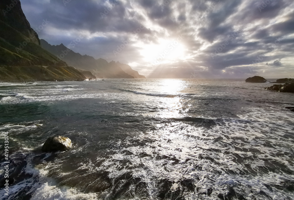 Obraz premium Stunning sunset view in the ocean bay with mountains, , waves and sunbeams playing on them