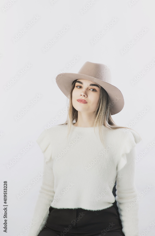girl in a white sweater posing in a felt hat on a light background girl in a white sweater posing in a felt hat on a light background
