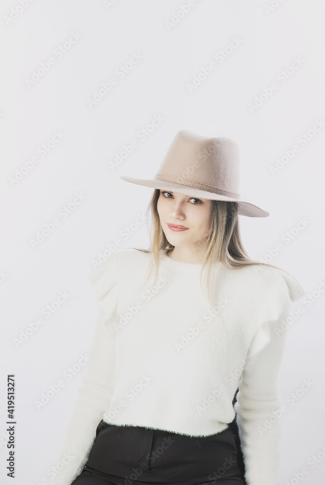 girl in a white sweater posing in a felt hat on a light background girl in a white sweater posing in a felt hat on a light background