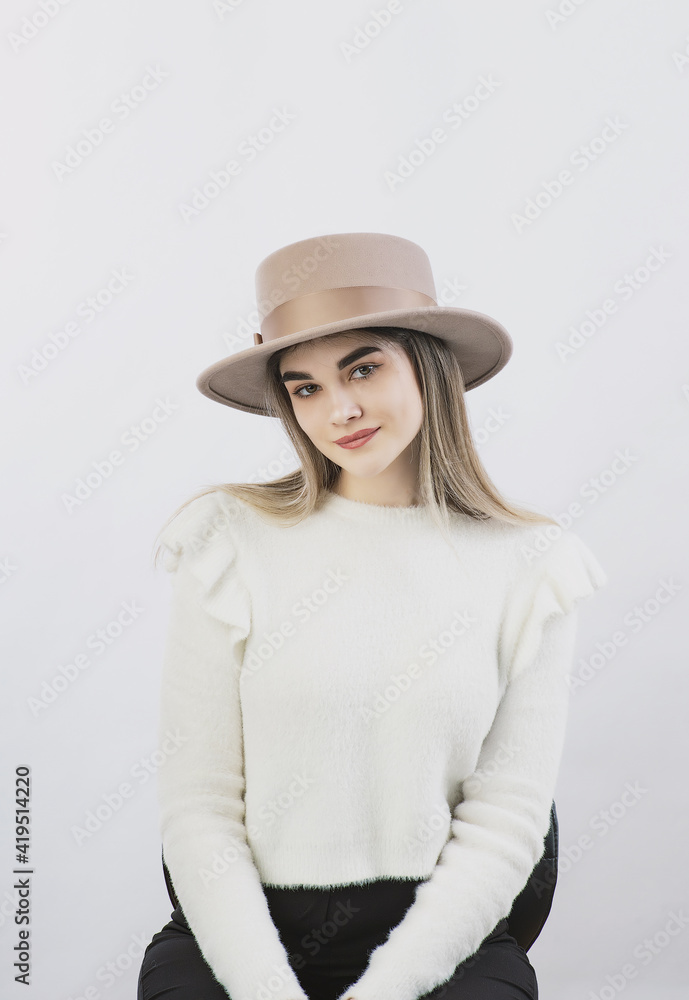 girl in a white sweater posing in a felt hat on a light background girl in a white sweater posing in a felt hat on a light background