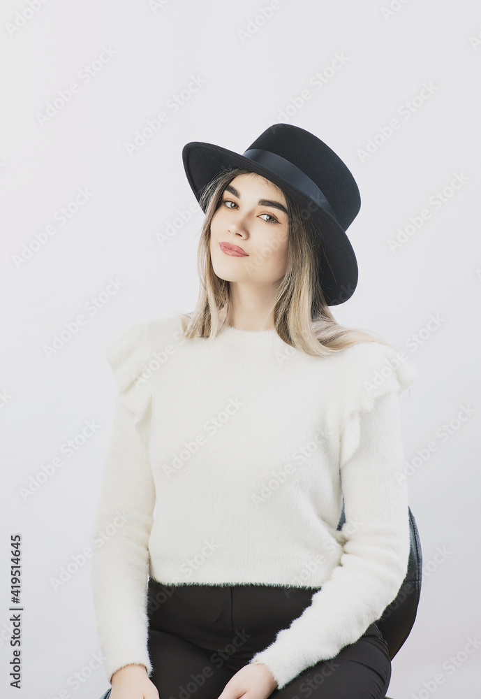 girl in a white sweater posing in a felt hat on a light background girl in a white sweater posing in a felt hat on a light background