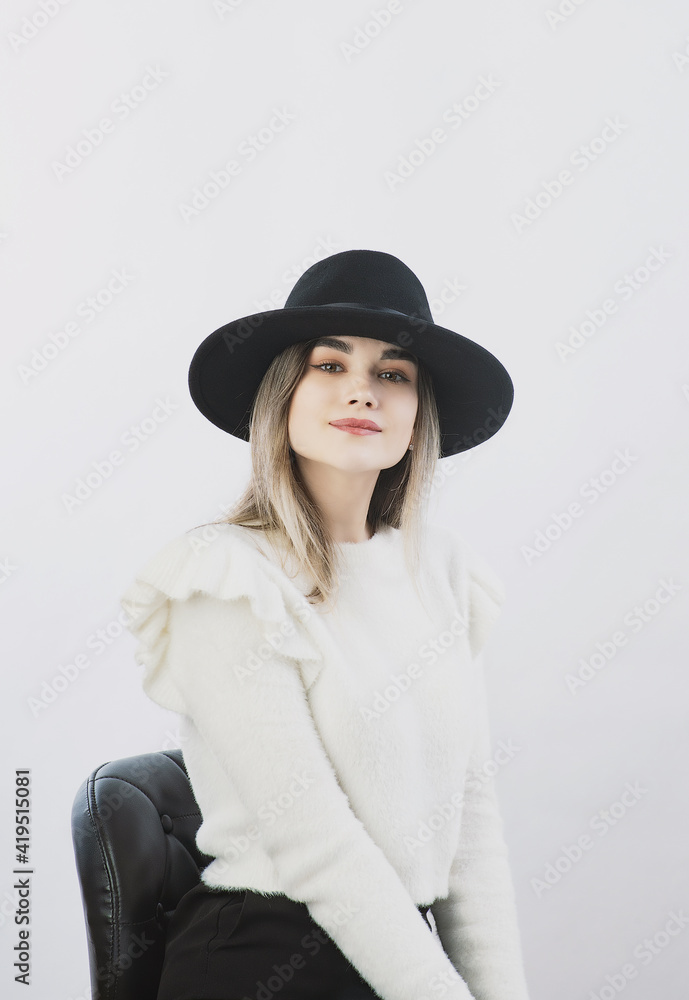 girl in a white sweater posing in a felt hat on a light background girl in a white sweater posing in a felt hat on a light background