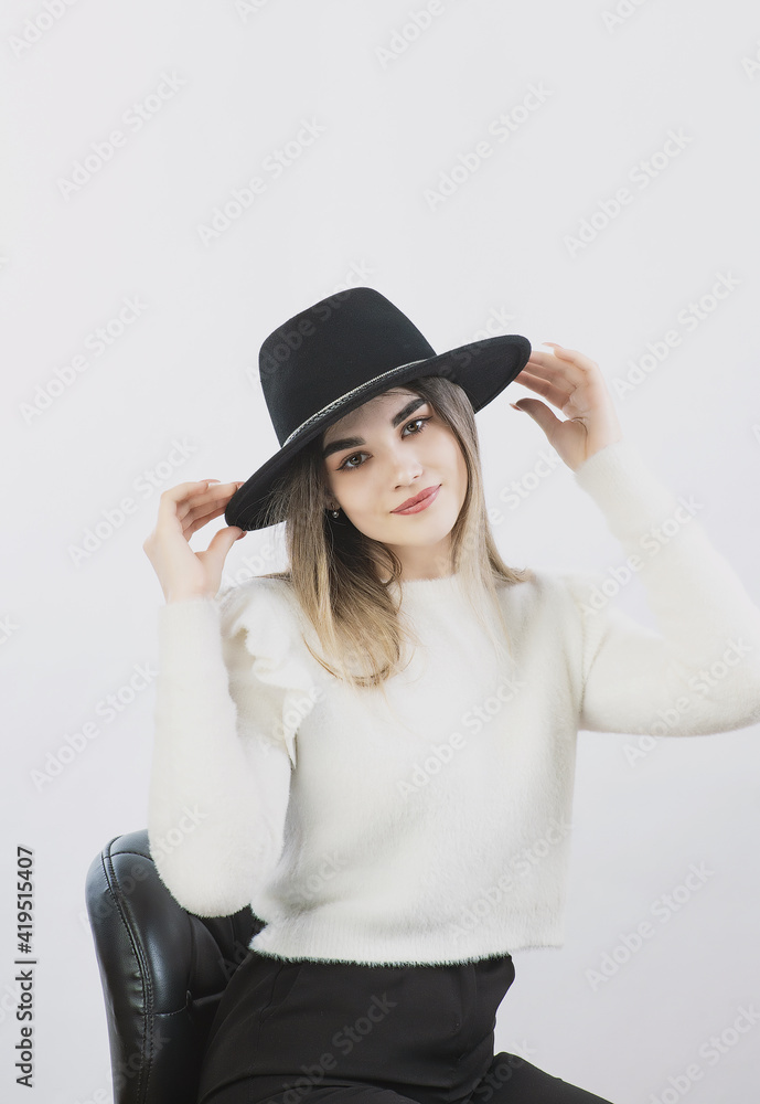 girl in a white sweater posing in a felt hat on a light background girl in a white sweater posing in a felt hat on a light background