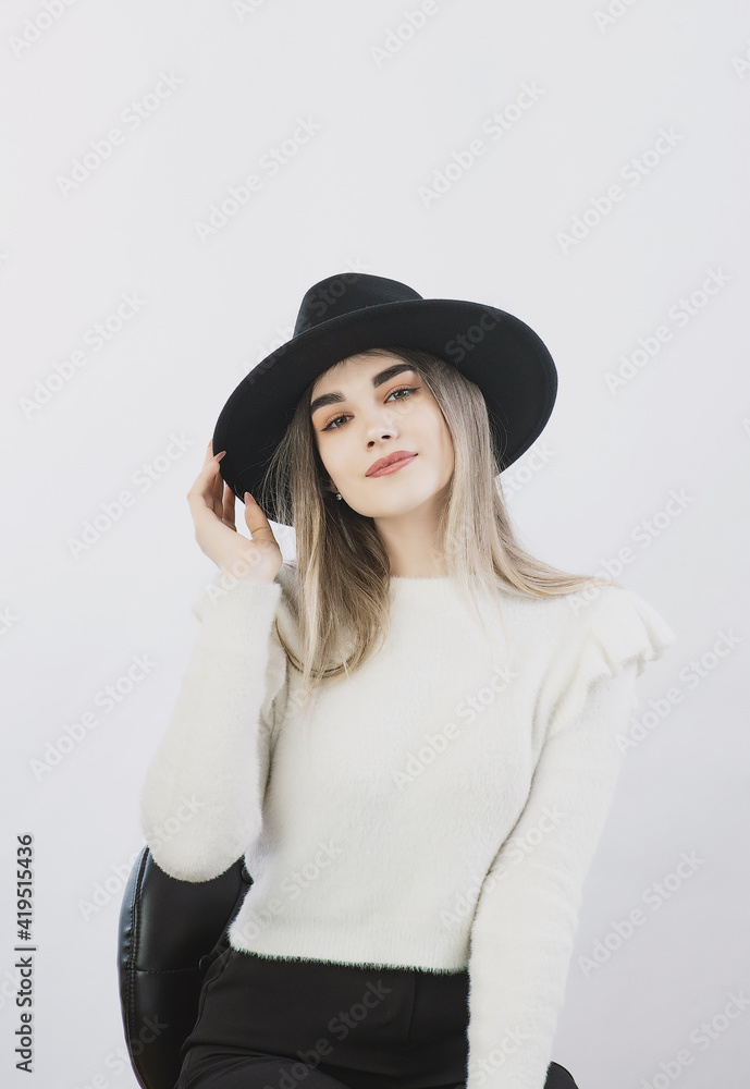 girl in a white sweater posing in a felt hat on a light background girl in a white sweater posing in a felt hat on a light background