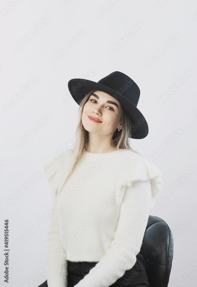 girl in a white sweater posing in a felt hat on a light background girl in a white sweater posing in a felt hat on a light background