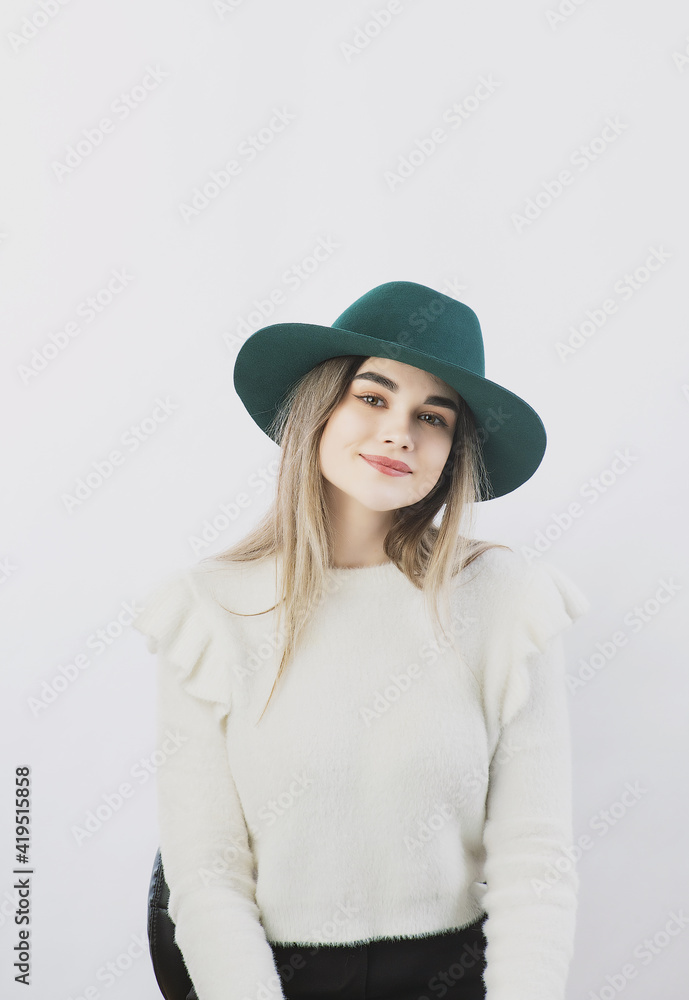girl in a white sweater posing in a felt hat on a light background girl in a white sweater posing in a felt hat on a light background