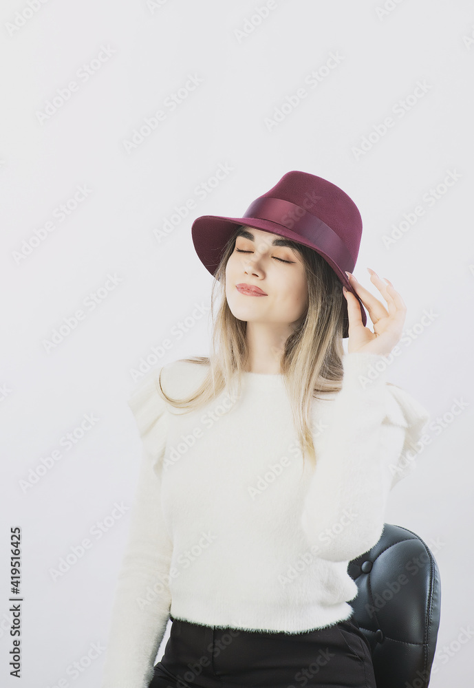 girl in a white sweater posing in a felt hat on a light background girl in a white sweater posing in a felt hat on a light background