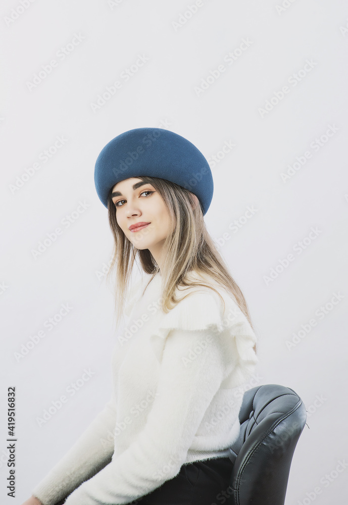 girl in a white sweater posing in a felt hat on a light background girl in a white sweater posing in a felt hat on a light background