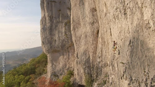 AERIAL: Flying past a fearless male rock climber ascending up a cliff in rural Slovenia on an idyllic autumn day. Athletic man climbs a challenging rock wall in Crni Kal on a beautiful day in fall.