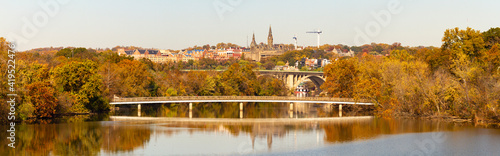 An autumn landscape panorama of Potomac river Theodore Roosevelt Island (left) and a small pedestrian bridge is seen. Francis Scott Key Memorial Bridge and Georgetown University is in the background.