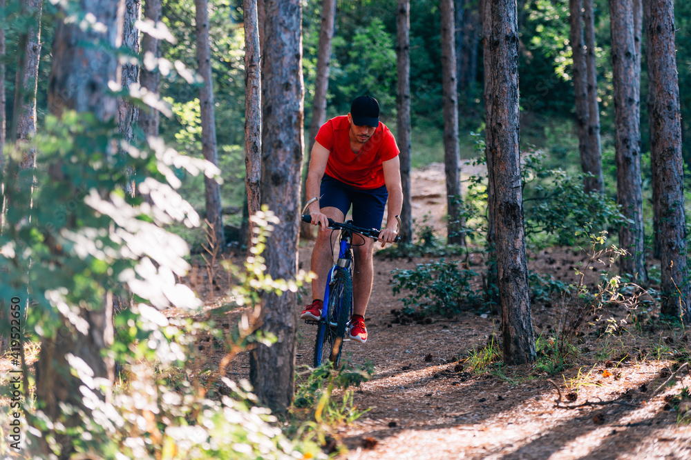 Fit cyclist riding his bike downhill through a forest ( woods ) while wearing a red shirt and red shoes. Fit cyclist riding his bike downhill through a forest ( woods ) while wearing a red shirt and red shoes.