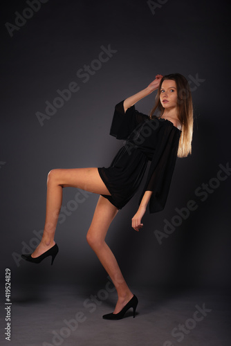 Full-length picture of an attractive sexy young female model posing isolated on a dark background with black dress