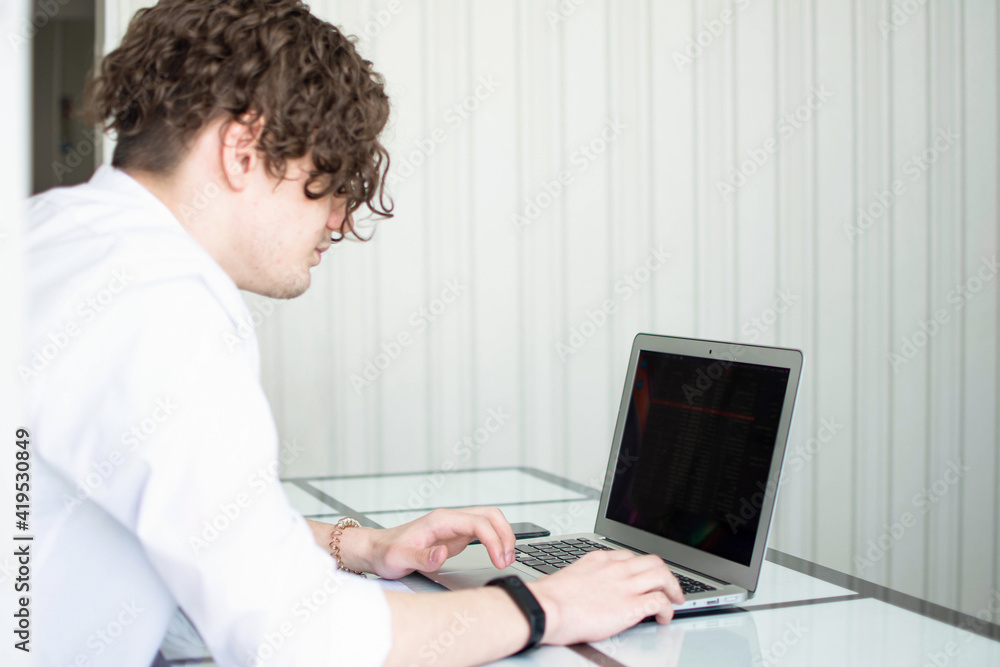 Caucasian man with curly hair working at the laptop. copy space. side view. horizontal. Caucasian man with curly hair working at the laptop. copy space. side view. horizontal.