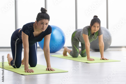 Focus to adults asian woman wearing blue sport suit are crawl on green carpet do yoga exercise in the morning and sunlight with blue and gray fit ball exercise near window in background