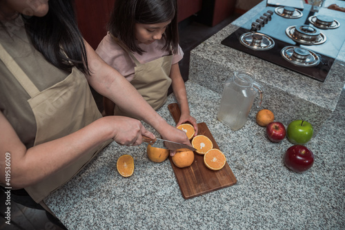 Mexican mother and daughter preparing orange juice in the kitchen, close uo