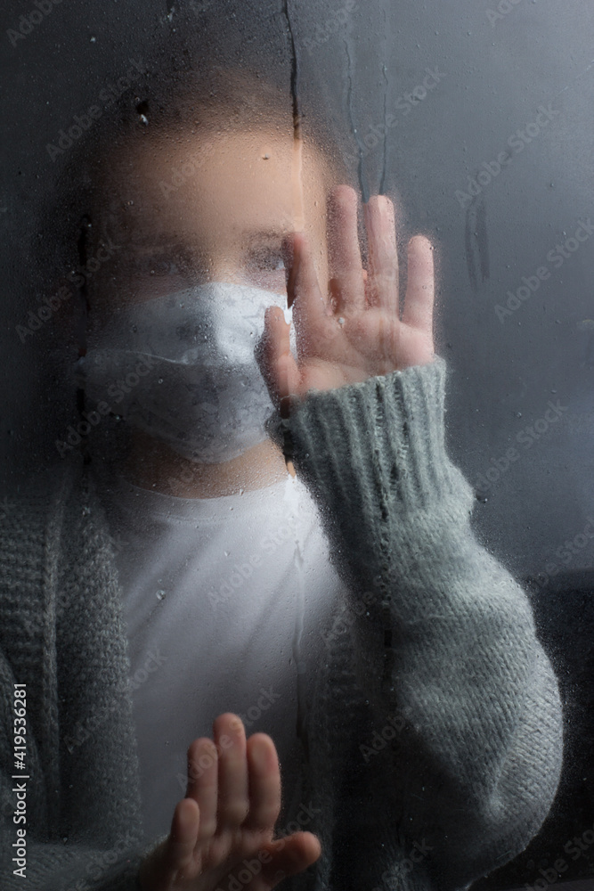 A young boy stands at the window with a raindrop on the glass after the rain. A young boy stands at the window with a raindrop on the glass after the rain.