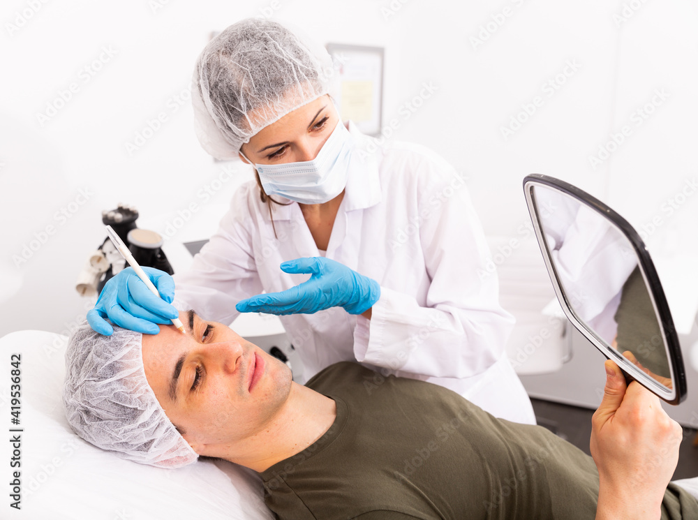 Naklejka premium Confident woman cosmetologist examining male client face before procedure in esthetic clinic