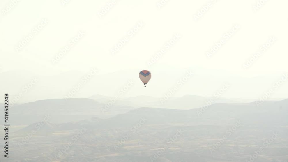 Large colourful alone hot air balloon with basket silhouette flies over white misty mountainous landscape in early autumn morning. Large colourful alone hot air balloon with basket silhouette flies over white misty mountainous landscape in early autumn morning.