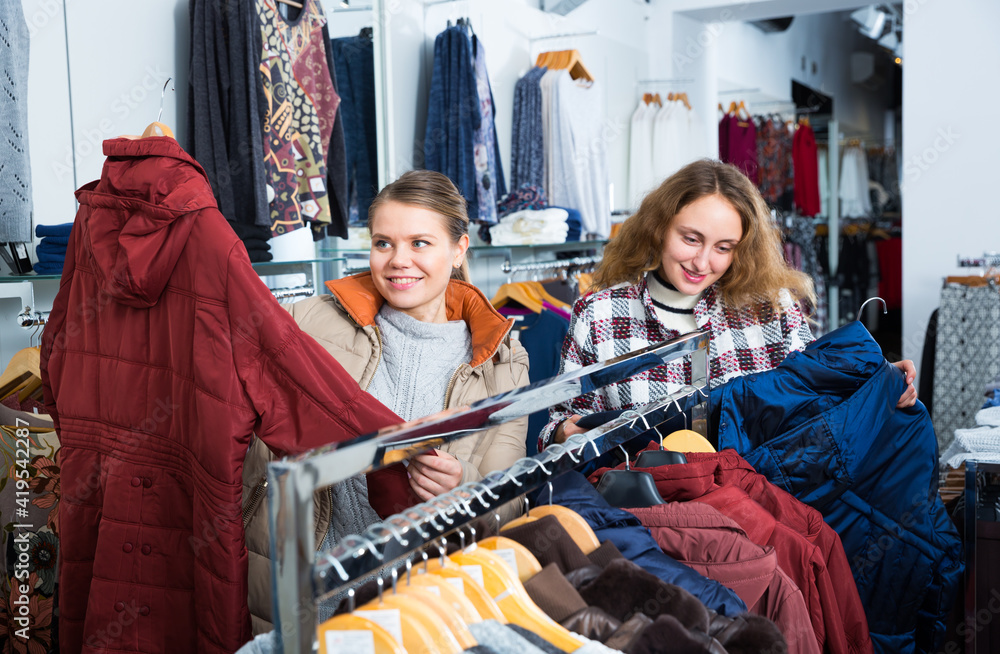 Obraz premium Two young cheerful women shopping in outerwear clothing boutique