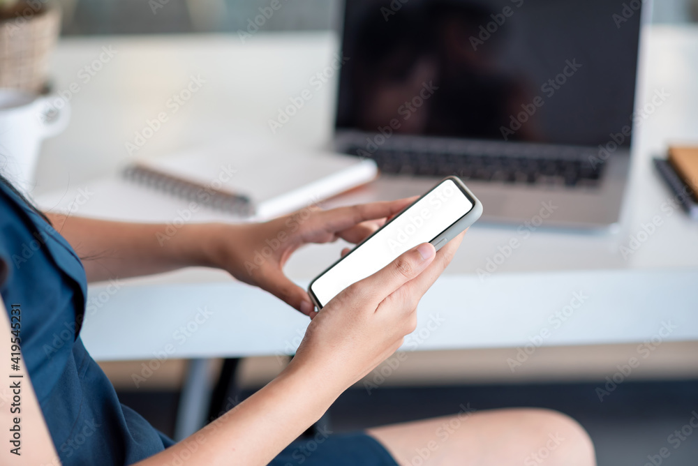 Image of a businesswoman holding smartphone white blank screen laptop placed on an office table. Mock up. Image of a businesswoman holding smartphone white blank screen laptop placed on an office table. Mock up.