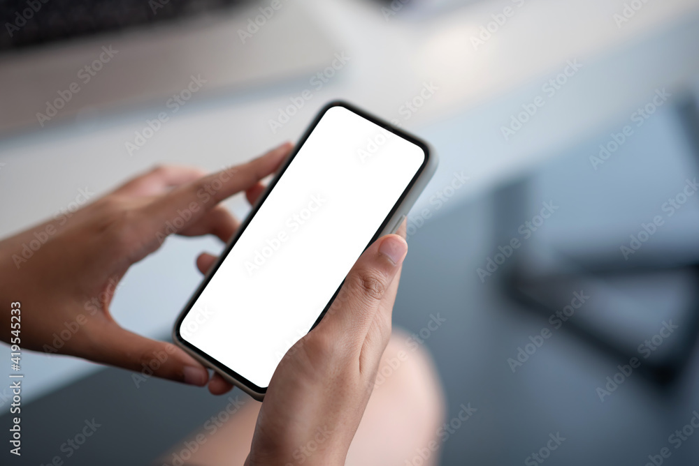 Image of a businesswoman holding mobile phone white blank screen at the office. Mock up.