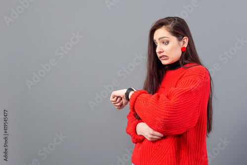busy woman in red sweather worried looking at her wristwatch, isolated on gray background