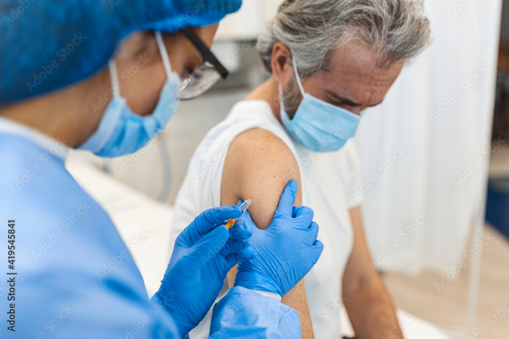 Close up of general practitioner hand holding vaccine injection while wearing face protective mask during covid-19 pandemic. Young woman nurse with surgical mask giving injection to senior man.