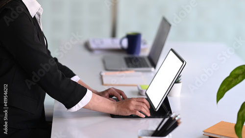 Side view businesswoman typing on keyboard of computer tablet while sitting in meeting room.