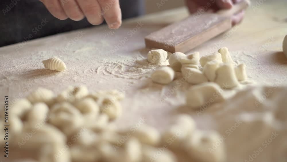 Close up process of homemade vegan tradition italian potatoes gnocchi pasta. Expert-aged cook shapes the dough with special manual tool the wooden chopping board. Man cooking food in the kitchen Close up process of homemade vegan tradition italian potatoes gnocchi pasta. Expert-aged cook shapes the dough with special manual tool the wooden chopping board. Man cooking food in the kitchen
