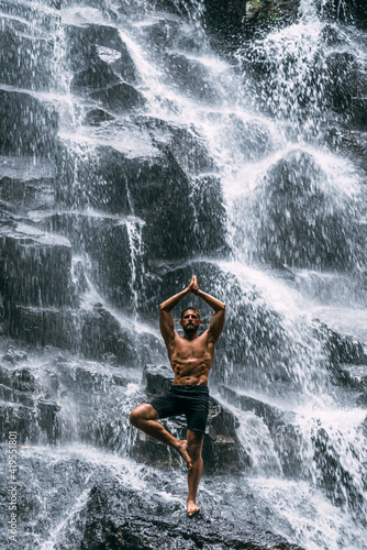Fototapeta Naklejka Na Ścianę i Meble -  A man of athletic build does yoga. Healthy lifestyle. The concentration of the body. A man does yoga at a waterfall. A man does yoga in Bali. A man meditates in nature. Meditation at the waterfall