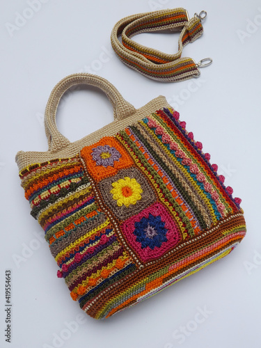 Image of colorful crochet bag made of leftover yarn. Isolated against white surface. Concept of creativity, something bright colorful, and utilization leftover things. Strap also appeared in frame.  photo