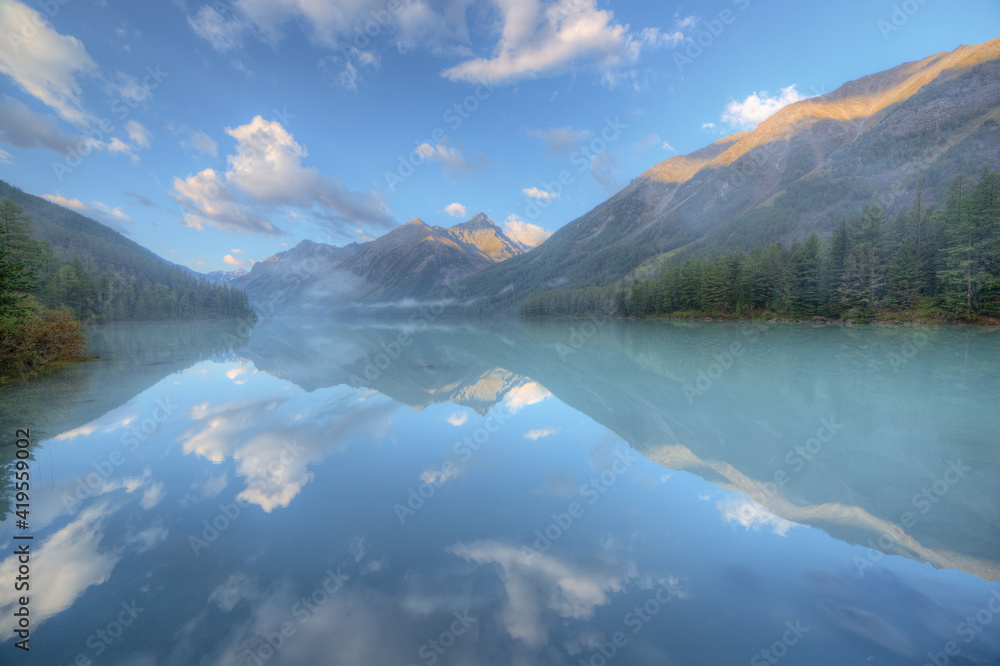 A beautiful lake in a mountain valley. Blue sky and clouds. Soft focus mountains and trees. Super wide angle.