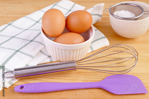 Eggs with a whisk and kitchen utensils on wooden table for home-cooking