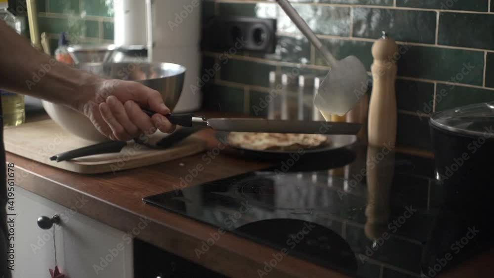 Cooking pancakes in the home kitchen in the morning. A man bakes thin Russian pancakes in a pan. Home cooking and food Cooking pancakes in the home kitchen in the morning. A man bakes thin Russian pancakes in a pan. Home cooking and food