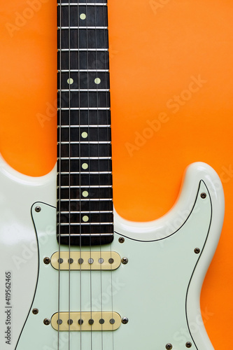 Detail of White Electric Guitar on a orange background.