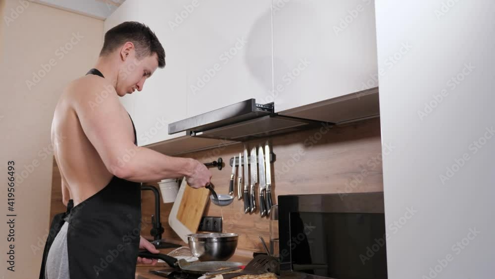 man with a naked torso and in a black apron prepares pancakes in kitchen. man with a naked torso and in a black apron prepares pancakes in kitchen.