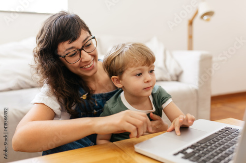 Mãe autônoma e filho sorrindo trabalhando no computador em casa