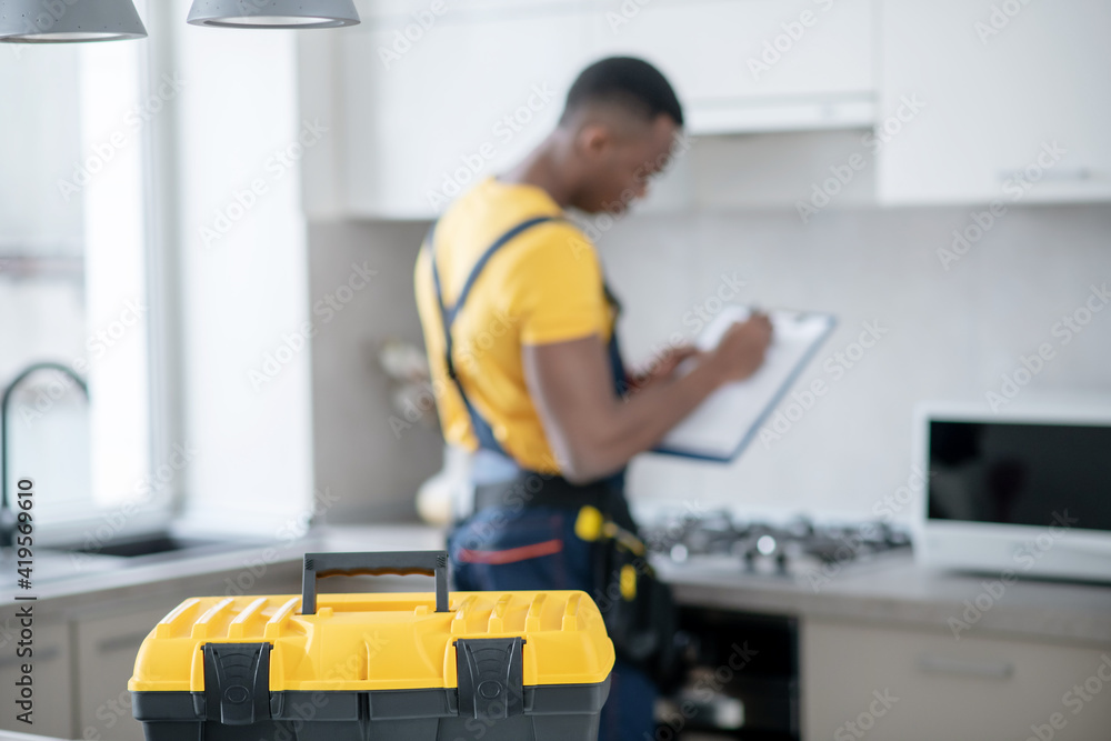 Dark-skinned service man standing in the kitchen and making notes Dark-skinned service man standing in the kitchen and making notes