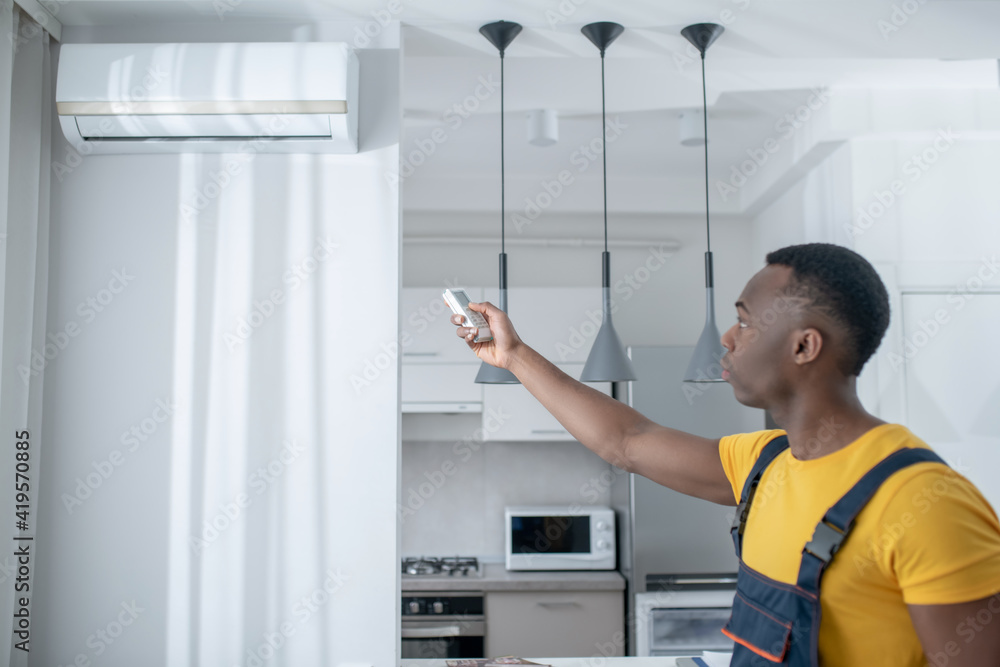 Dark-skinned service man in yellow tshirt installing the air-conditioner Dark-skinned service man in yellow tshirt installing the air-conditioner