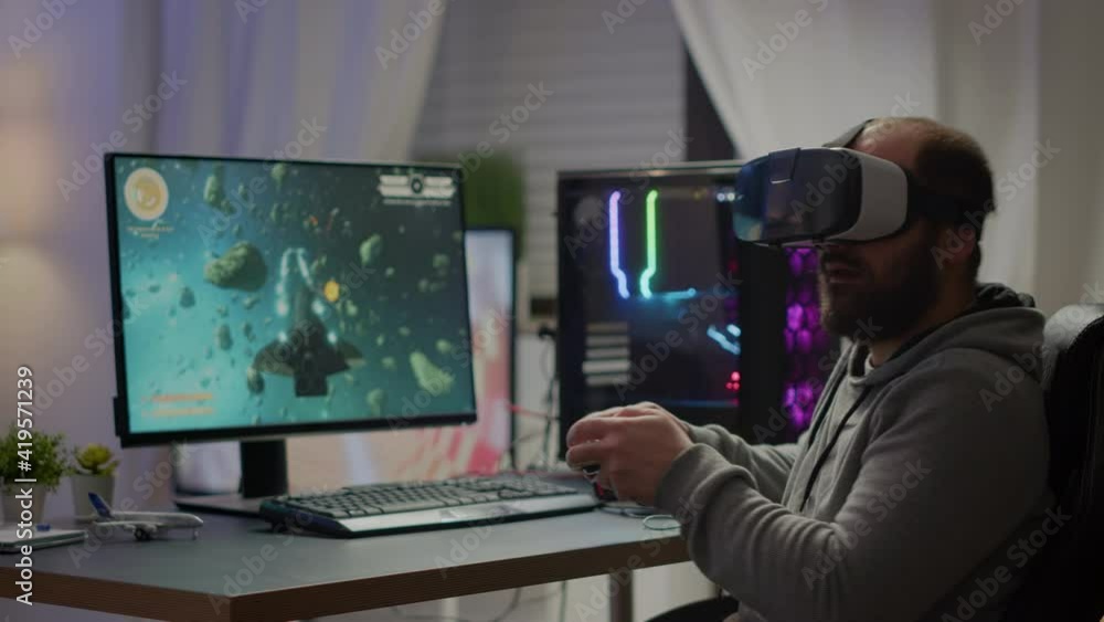 Videogame player with VR headset raising hands after winning space shooter competition. Professional pro gamer playing online video games with new graphics on powerful computer from gaming room Videogame player with VR headset raising hands after winning space shooter competition. Professional pro gamer playing online video games with new graphics on powerful computer from gaming room