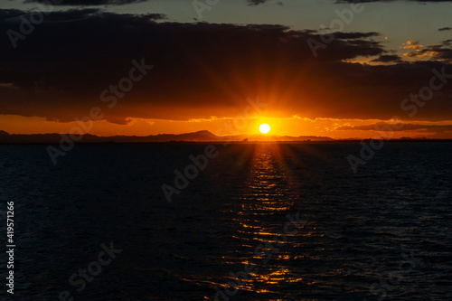colorful low keyl sunset over the ocean with shimmering light on the waves and silhouette of mountains on the shore behind