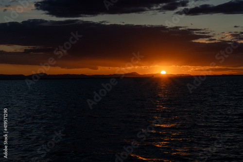 colorful low keyl sunset over the ocean with shimmering light on the waves and silhouette of mountains on the shore behind