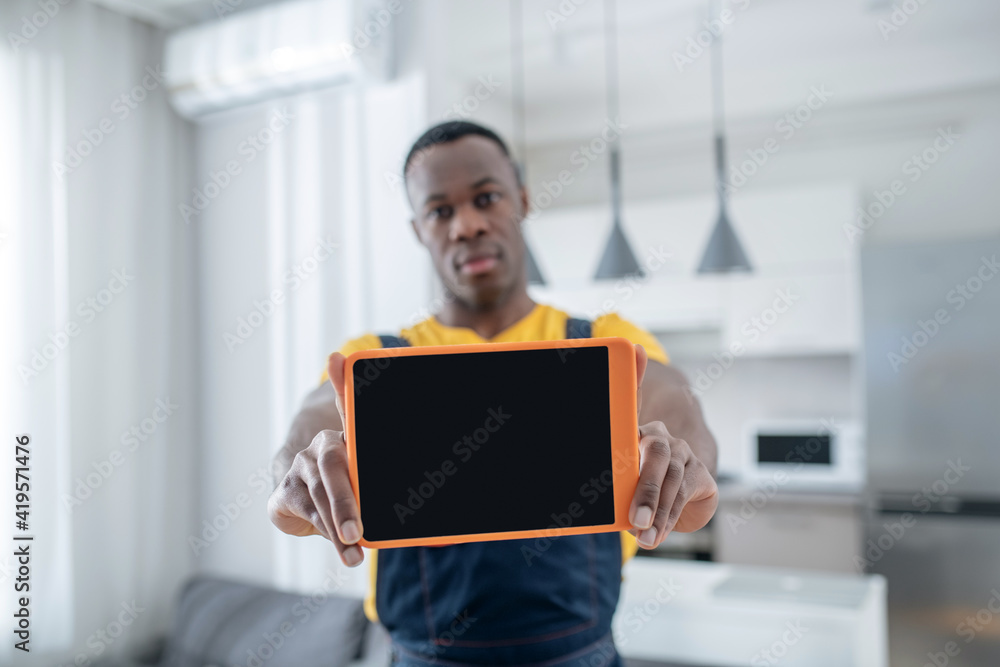 Dark-skinned service man in yellow tshirt holding a tablet
