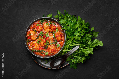 Chicken Vindaloo with spinach in black bowl on dark slate table top. Indian cuisine meat chilli curry dish. Authentic asian food. Top view photo