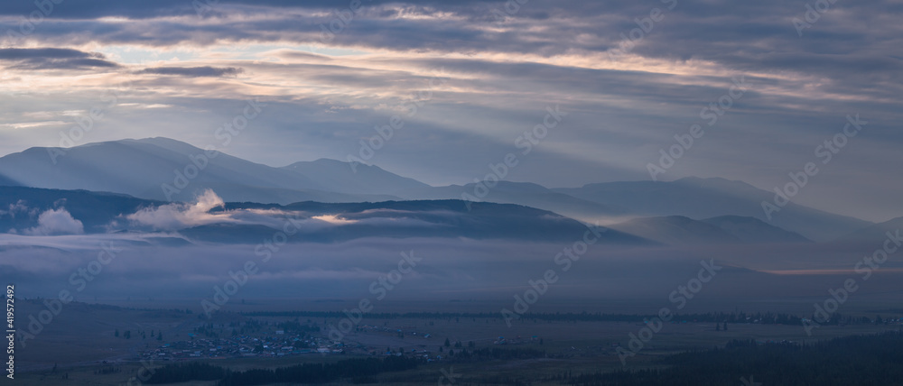 Dawn in the mountains, peaks above the clouds, foggy. Panoramic view.