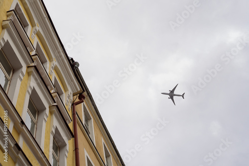 View to flying plane in sky from below. Aircraft over city buildings