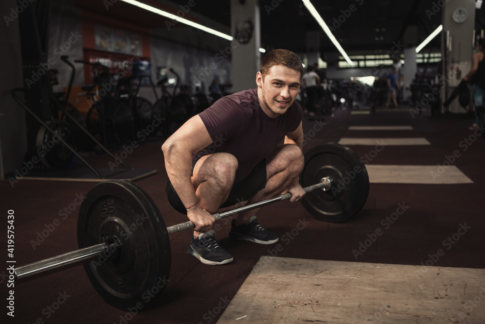 Happy handsome athlete smiling to the camera while working out with barbell Happy handsome athlete smiling to the camera while working out with barbell