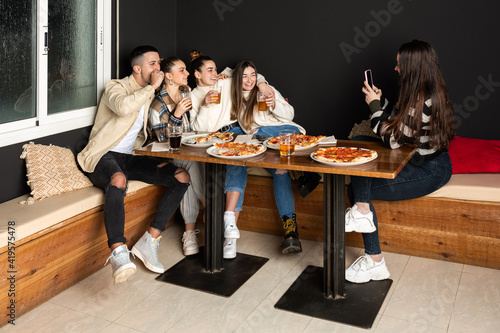 groups of young people take a selfie photo while eating pizzas at a restaurant