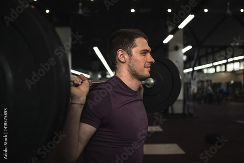 Cheerful handsome sportsman smiling, wnjoying working out with heavy barbell photo